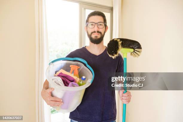 young latin man performing cleaning in empty apartment. - holding broom stock pictures, royalty-free photos & images