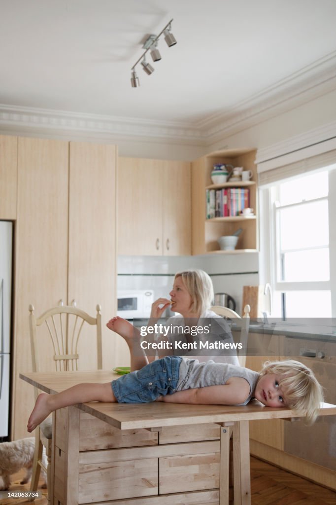 Child lying on kitchen table, mum in background