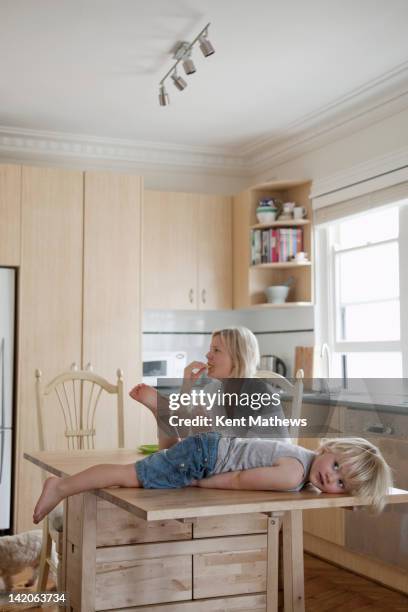 Child Lying On Kitchen Table Mum In Background, Foto de stock