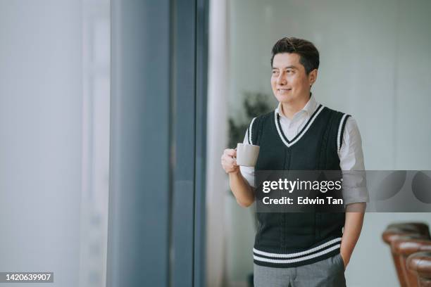 asian chinese businessman looking away smiling standing beside window in meeting room - wealthy man stock pictures, royalty-free photos & images