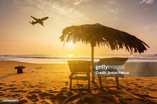 beach at a tropical resort at sunset and a flying plane. summer vacation on tropical resort - beach plane stock pictures, royalty-free photos & images