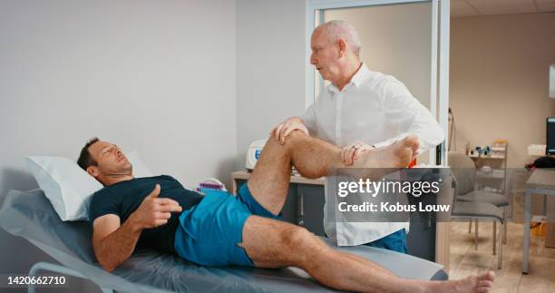physiotherapist doing exercise with man after leg injury, stretching during physiotherapy consultation and doing healthcare checkup with doctor at hospital. man doing feet training with worker - human joint stock pictures, royalty-free photos & images