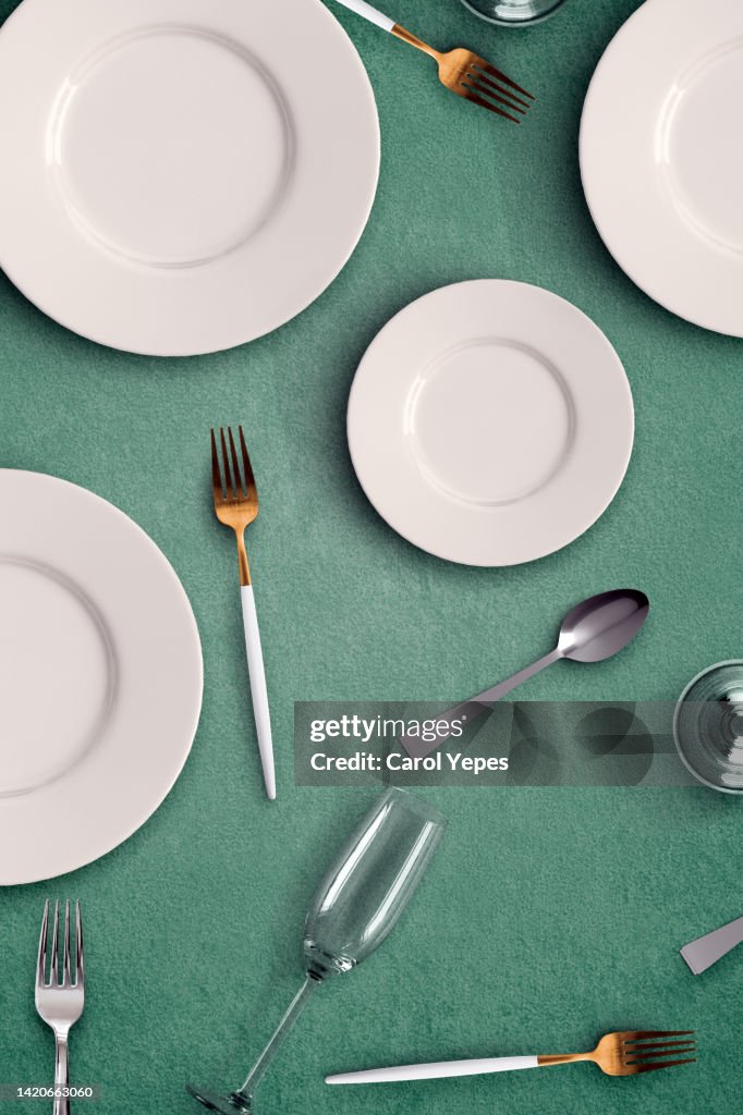Empty plate table setting i with forks, spoons, glasses in green background