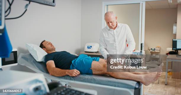 physiotherapist doctor with patient in physical therapy for legs or muscle pain in a hospital exam consultation. senior healthcare professional doing examination of of sports man on orthopedic table - human arm anatomy stock pictures, royalty-free photos & images