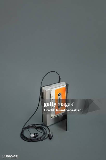 gray portable analog audio cassette player with wired black earbuds and white cassette tape with orange label inside on gray background. with copy space on the top. - leitor de cd portátil imagens e fotografias de stock