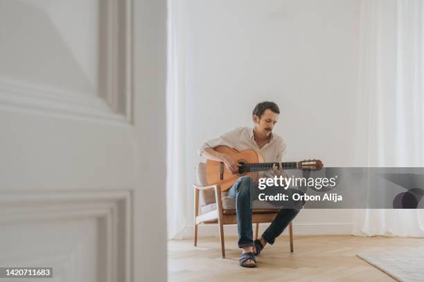 man playing guitar in the living room - acoustic guitarist stock pictures, royalty-free photos & images