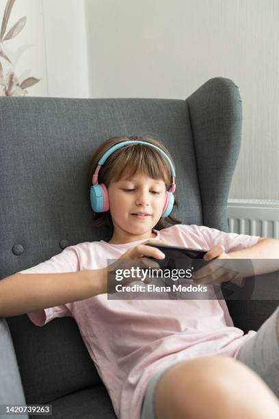 a charming teenage girl in wireless headphones and with a mobile phone in her hands sits on an armchair. use of gadgets by children - salazar bronwich testify at hearing on re organization of mms stockfoto's en -beelden