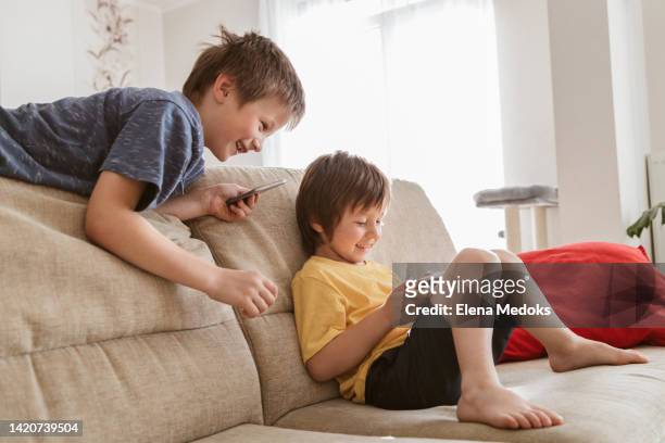 two boys, brothers play video games on mobile phones in the living room on the sofa. - game six stockfoto's en -beelden