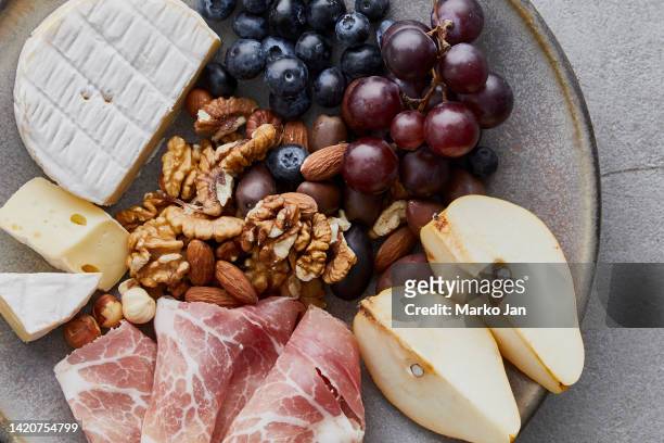 cheese plate with prosciutto, pears, nuts and grapes - cheese platter stock pictures, royalty-free photos & images