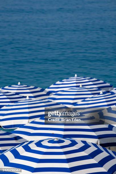 blue striped beach umbrellas against a blue sea - parasol persoonlijk accessoire stockfoto's en -beelden