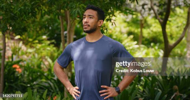 joven corredor en un parque o naturaleza con árboles de fondo tomando un descanso durante una sesión de entrenamiento y pensando en un objetivo de acondicionamiento físico. atleta o deportista que respira aire fresco antes de entrenar ejercicio - mano sobre la cadera fotografías e imágenes de stock