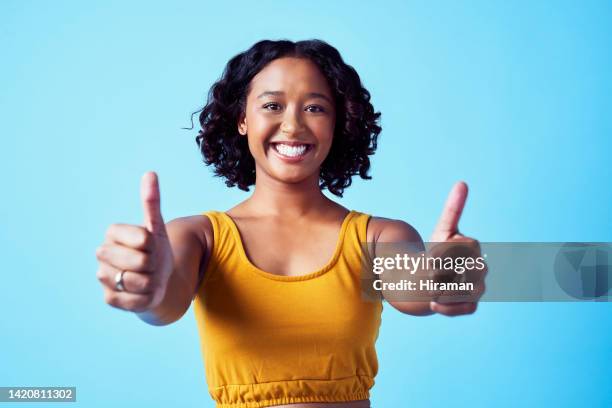 pulgares hacia arriba, motivación y éxito con una mujer dando una sonrisa y un gesto con la mano en el estudio aislado sobre un fondo azul. gracias, ganador y sí con una persona feliz diciendo que sí de acuerdo y confianza - thank you fotografías e imágenes de stock