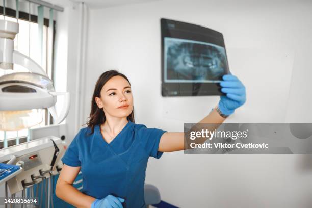 young female dentist examining an x ray image of patient mouth - dental assistant stock pictures, royalty-free photos & images