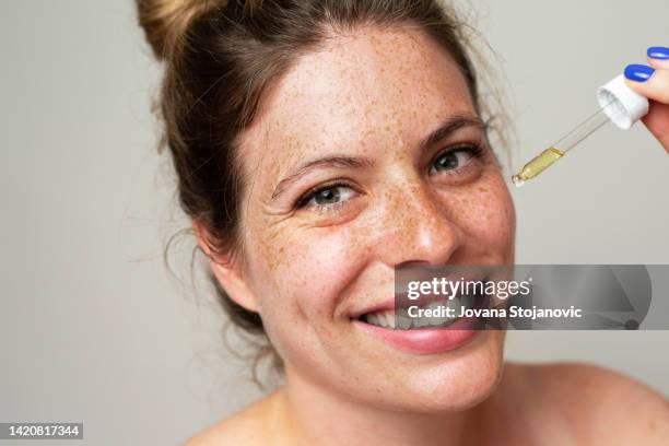 a beautiful woman with freckles applies serum to her face with a pipette - retinol stock pictures, royalty-free photos & images
