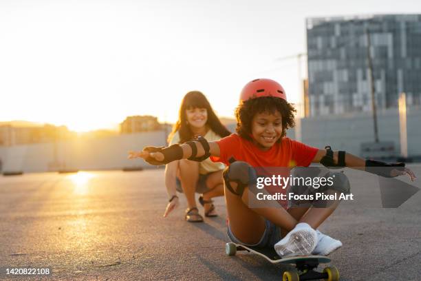 mother pushing her daughter on a skateboard. - monopatín artículos deportivos fotografías e imágenes de stock