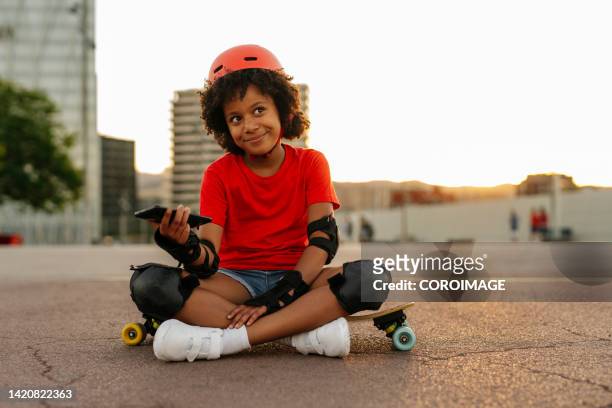 8-year-old girl sitting on a skateboard with a smartphone in her hands. - 8 girls no cup stock-fotos und bilder