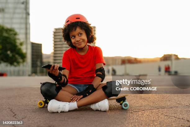 8-year-old girl sitting on a skateboard with a smartphone in her hands. - sports helmet - fotografias e filmes do acervo