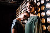 Female portrait of two fashion woman at the backstage of fashion week show. Lifestyle photography, behind the scenes of new clothing collection. Girls wear by fashion designer. Wall with lights