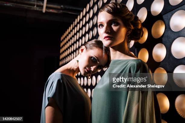female portrait of two fashion woman at the backstage of fashion week show. lifestyle photography, behind the scenes of new clothing collection. girls wear by fashion designer. wall with lights - fashion show 個照片及圖片檔