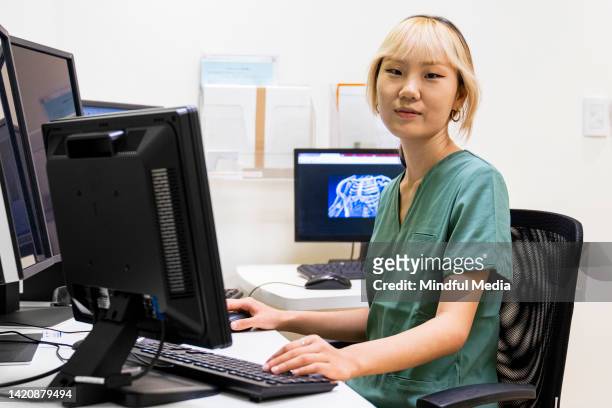 female asian-american diagnostic imaging operator checking data on monitors - department of health stock pictures, royalty-free photos & images