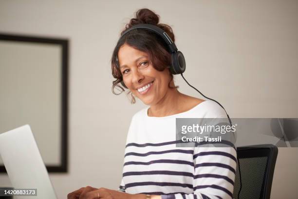 laptop, music and blog for mature woman working from home in house or living room. smile portrait, happy and creative designer, blogger or freelancer writing book and listening to radio on headphones - 50s woman writing at table imagens e fotografias de stock