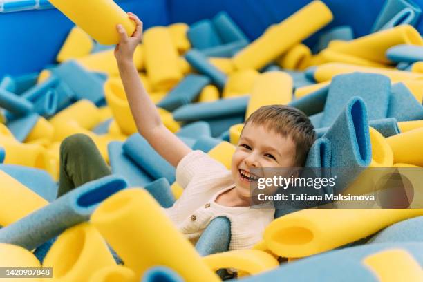 little boy  having fun at indoors playground. pool with soft tubes, front view. - indoor kids play area stock-fotos und bilder