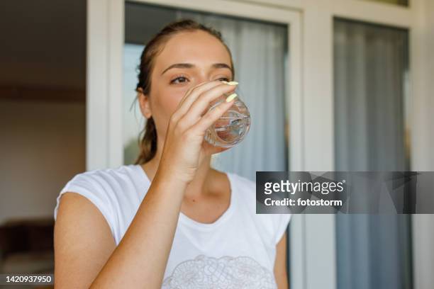 young woman drinking a glass of water after taking a pill to soothe her headache - sachet stockfoto's en -beelden