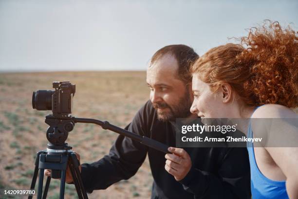 man and woman working together with camera on a tripod while making video content in nature - medienberuf stock-fotos und bilder