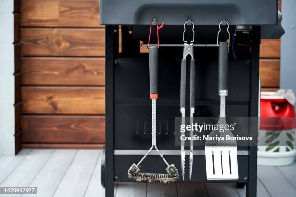 the grill utensils hang on the gas grill: a spatula, tongs, and a brush. - tongs work tool stock pictures, royalty-free photos & images