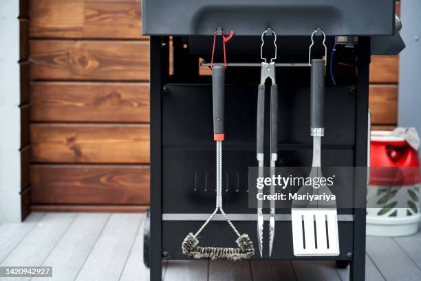the grill utensils hang on the gas grill: a spatula, tongs, and a brush. - pinça utensílio de servir - fotografias e filmes do acervo