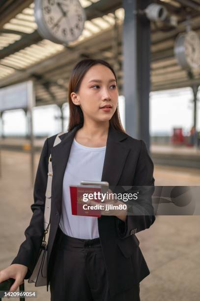 joven y hermosa mujer de negocios asiática sonríe y sostiene su teléfono y pasaporte en la plataforma del tren de cercanías esperando el tren - portraits of people passport fotografías e imágenes de stock