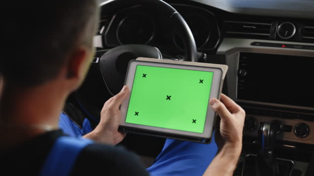 Unrecognizable vehicle service manager worker check and maintenance to repair the engine car in workshop. Mechanic running diagnostics software on tablet computer with green screen mockup chromakey