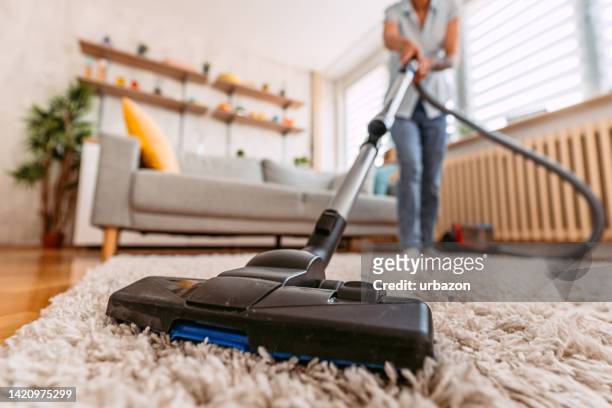 senior woman vacuuming her apartment - tapijt stockfoto's en -beelden