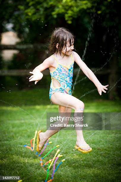 a five-year-old girl jumps through a sprinkler in her bathing suit in her back yard. - stamford connecticut stock pictures, royalty-free photos & images