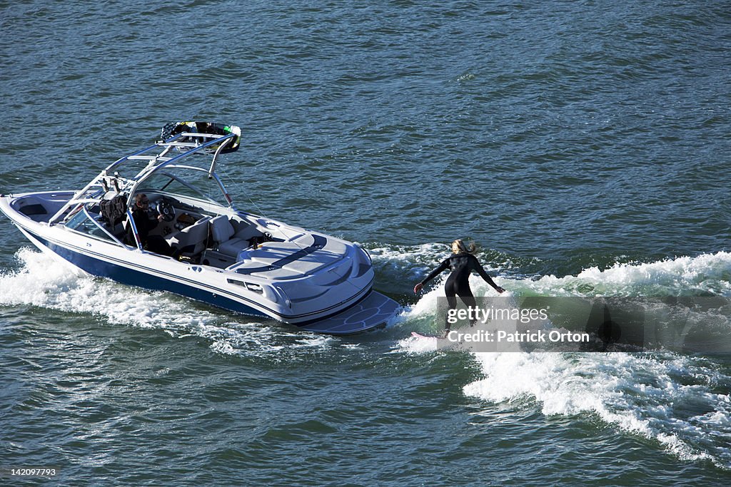A happy athletic woman wake surfs behind a wakeboard boat in Idaho.