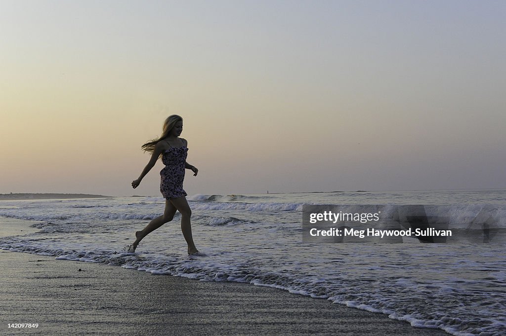 A young woman runs in the surf during sunset.