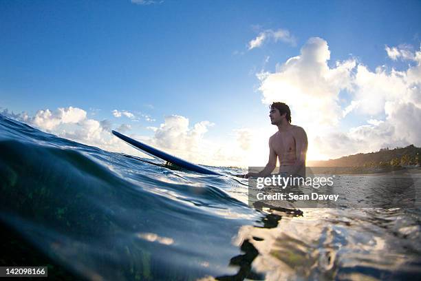 a young man surfing into the light at monster mush, on the north shore of oahu, hawaii. - sitting on surfboard ストックフォトと画像