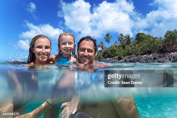 a split level view of a young family in the water at waimea bay. - waimea bay stock pictures, royalty-free photos & images