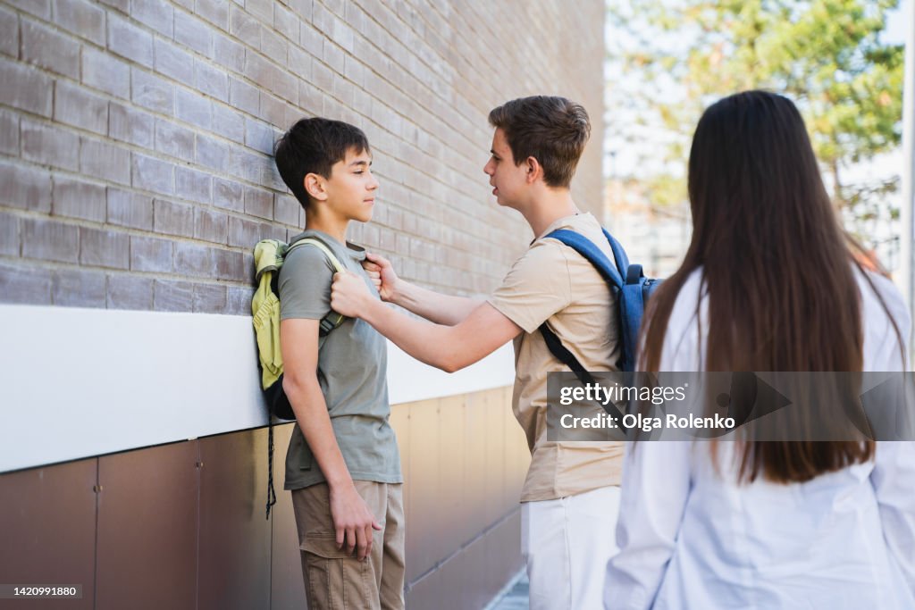 Teenager fighting, bullying and abuse. Abuser trying to fight, punching the boy near school building