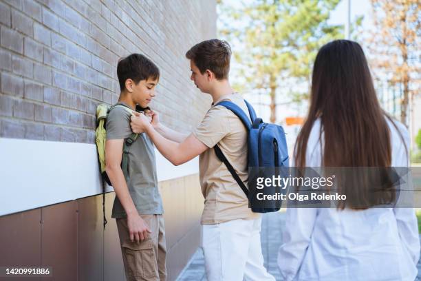 bullying and abuse in school. teen boy kicking, punching the boy near school building near classmate - kid punching stock pictures, royalty-free photos & images
