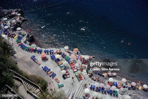 Elevated view looking down on sunbathers and parasols on the beach at La Scogliera beach in Positano, Italy, 1979.