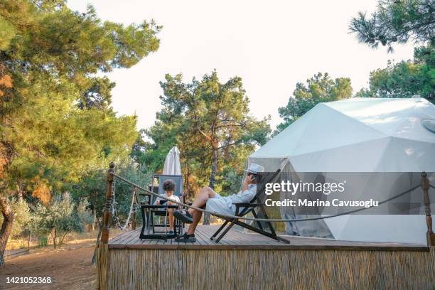 father and son sitting with his phone in glamping site. - idyllic cottage stock pictures, royalty-free photos & images