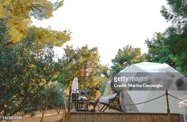 father and son sitting with his phone in glamping site. - luxury tent stock pictures, royalty-free photos & images