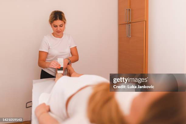 young beautician waxing young blonde woman's legs in a professional salon - wax fruit stock pictures, royalty-free photos & images