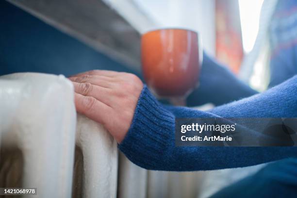 man with a cup of tea trying to warm up near a heater - no money stockfoto's en -beelden