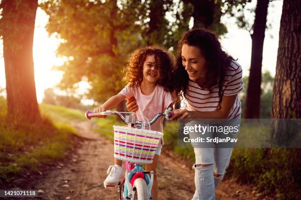 mutter, die ihrer tochter beibringt, wie man in der natur fahrrad fährt - bicycle daughter stock-fotos und bilder