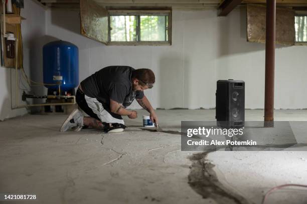 worker sealing basement floor cracks to protect house from mold. - stamped concrete stockfoto's en -beelden