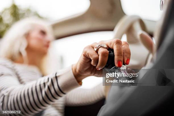 femme souriante assise sur le siège du conducteur dans sa voiture tenant le changement de vitesse - levier de vitesse photos et images de collection