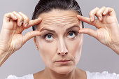 Woman checking wrinkles, doing antiaging face yoga exercises to firm and tighten skin.