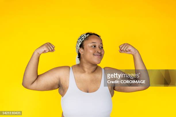 portrait of young woman in sportswear showing her strength on yellow background. - big fat women stock pictures, royalty-free photos & images